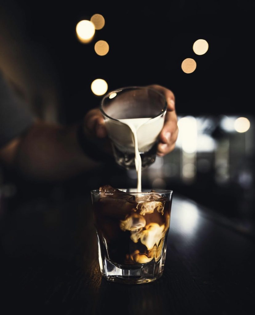pouring milk over iced coffee